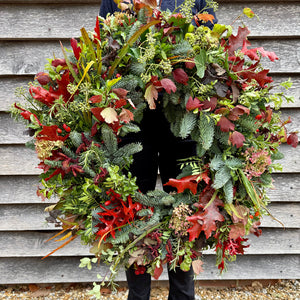 Person holding a large, colorful wreath against a wooden wall.