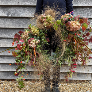 Person holding a large decorative wreath against a wooden wall.